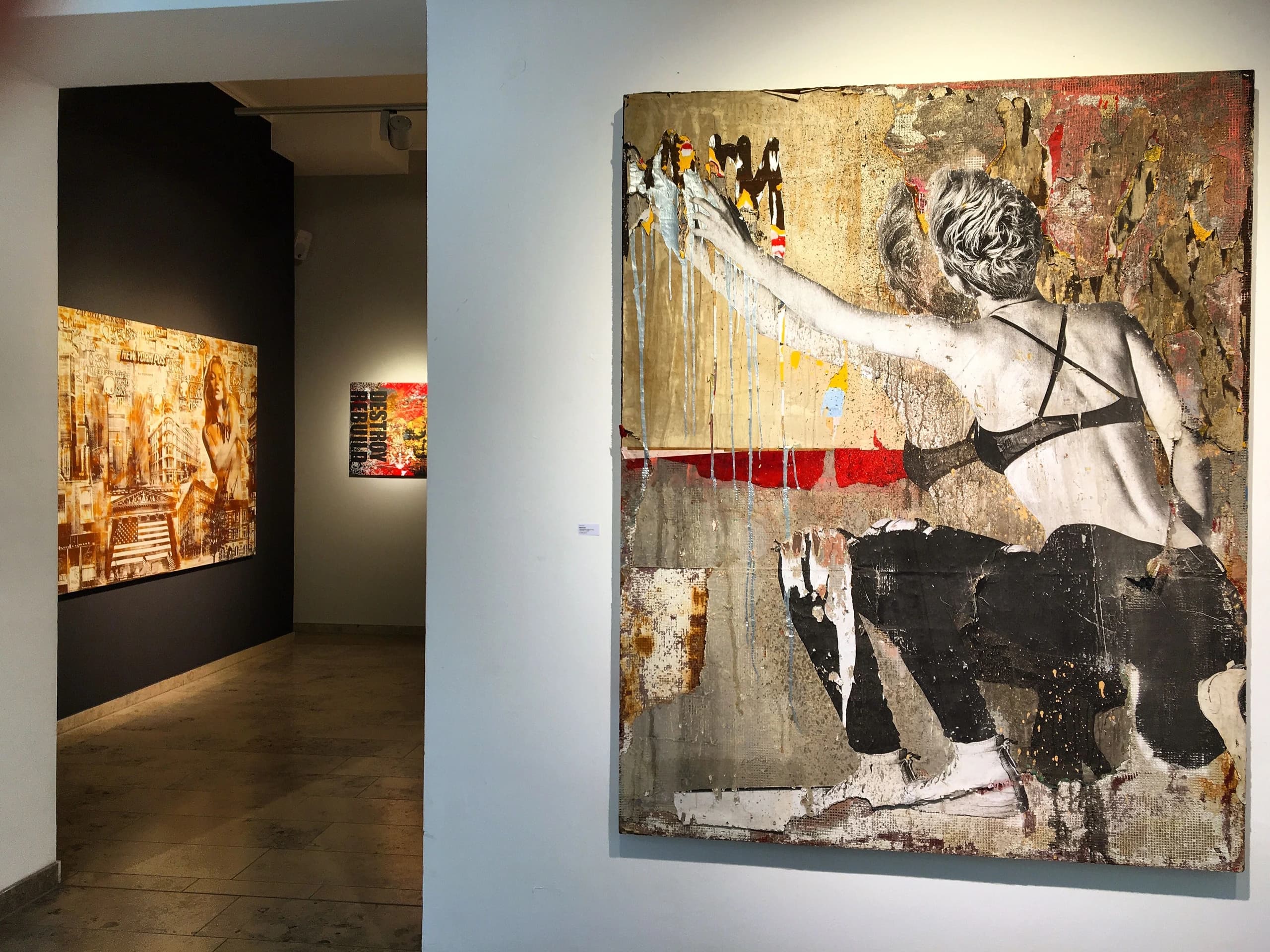 Galerieraum mit großem Wandbild einer knienden Frau rechts und weiteren Bildern an der dunklen Wand links.