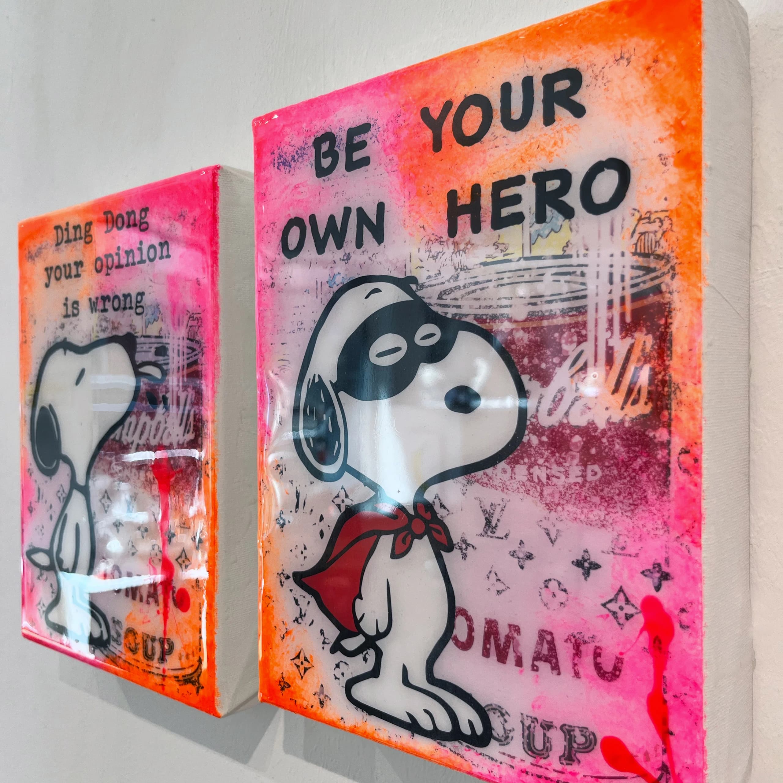 Zwei Leinwände mit Snoopy, rechts mit „BE YOUR OWN HERO“, links mit „Ding Dong your opinion is wrong“, in Pink und Orange.