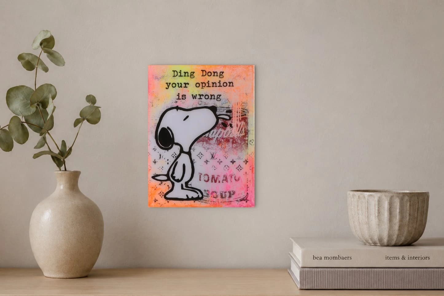 Snoopy vor einer Campbell’s Tomato Soup-Dose mit Schrift auf rosa-orangefarbenem Hintergrund, als Kunstwerk an der Wand eines hellen Raums.