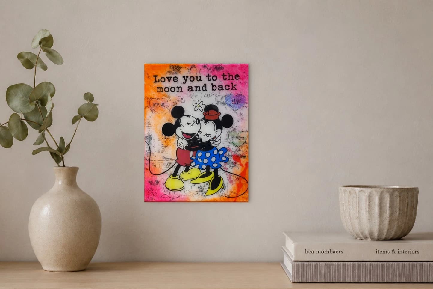 Mickey und Minnie umarmen sich vor buntem Hintergrund mit Text und Herzen, als Kunstwerk an der Wand eines hellen Raums.