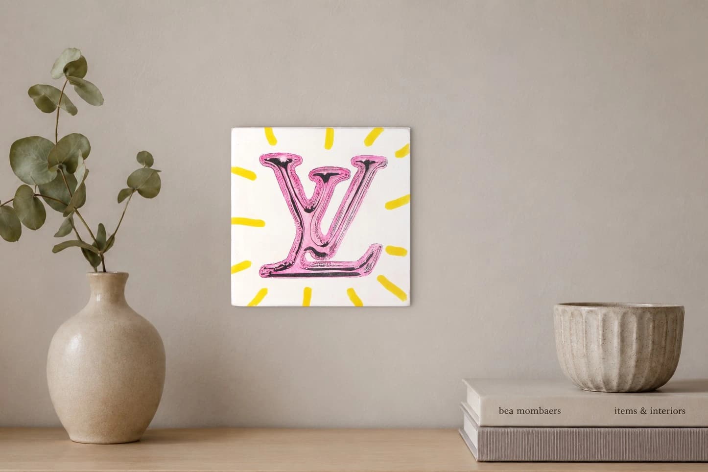 Großes pinkes LV-Logo auf weißem Grund mit gelben Strahlen, als Kunstwerk an der Wand eines hellen Raums.