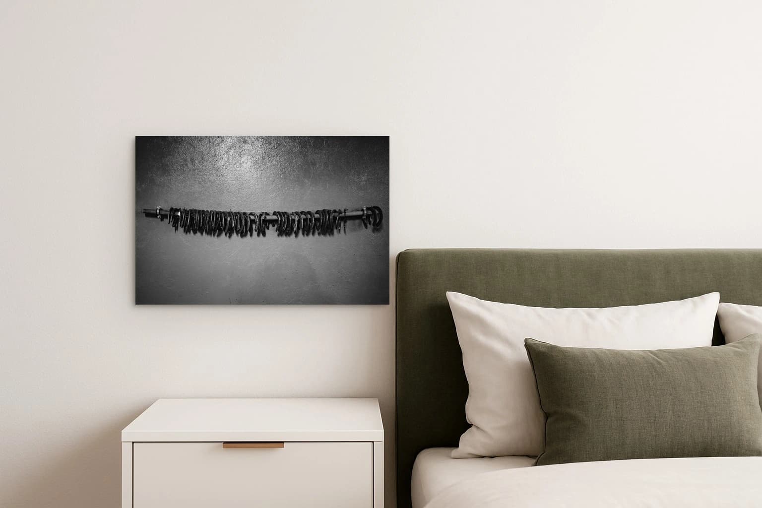Eine Reihe schwarzer Reifen hängt an einer Stange vor grauer Wand, als Kunstwerk an der Wand eines Schlafzimmers.