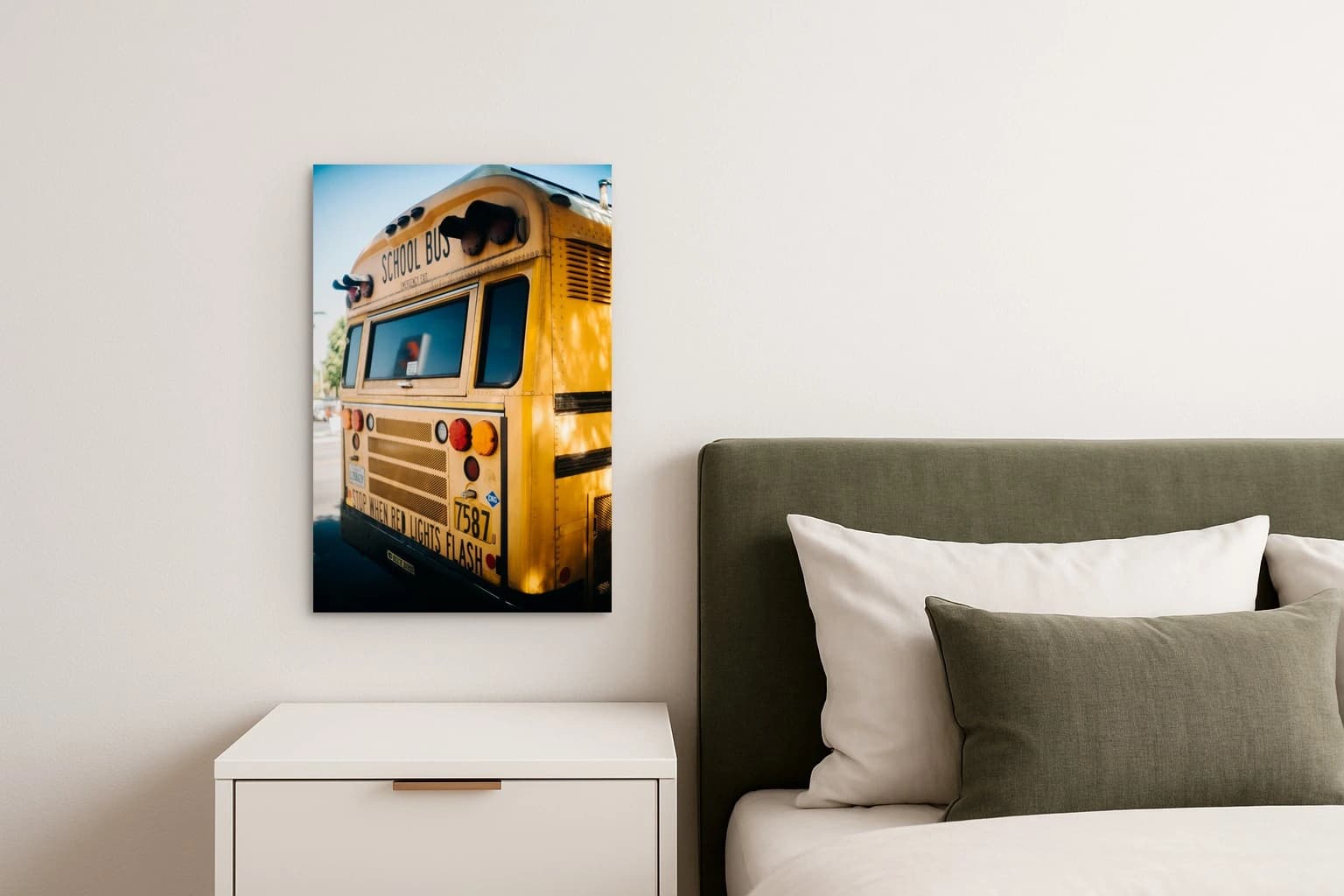 Gelber Schulbus von hinten mit SCHOOL BUS-Schrift und roten Lichtern auf einer Straße, als Kunstwerk an der Wand eines Schlafzimmers.