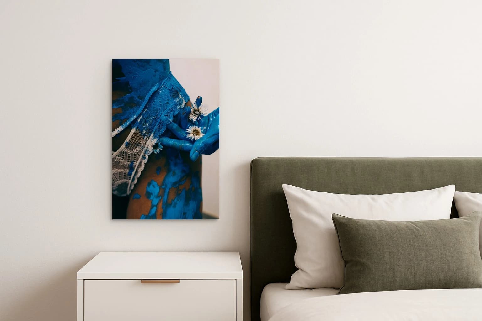 Blaue Hände halten weiße Blumen vor einem mit blauer Farbe bespritzten Oberkörper mit Spitze, als Kunstwerk an der Wand eines Schlafzimmers.