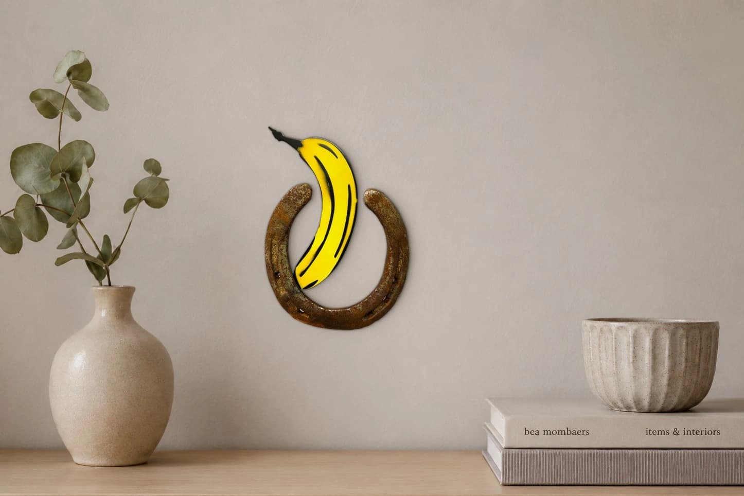 Gelbe Banane über rostigem Hufeisen auf schwarzem Hintergrund, als Kunstwerk an der Wand eines hellen Raums.