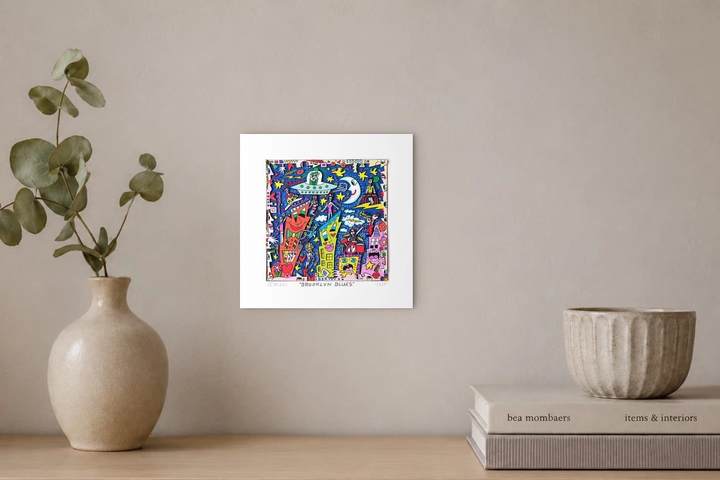 Bunte Comicfiguren und Häuser vor blauem Hintergrund in einem gerahmten Kunstdruck, als Kunstwerk an der Wand eines hellen Raums.
