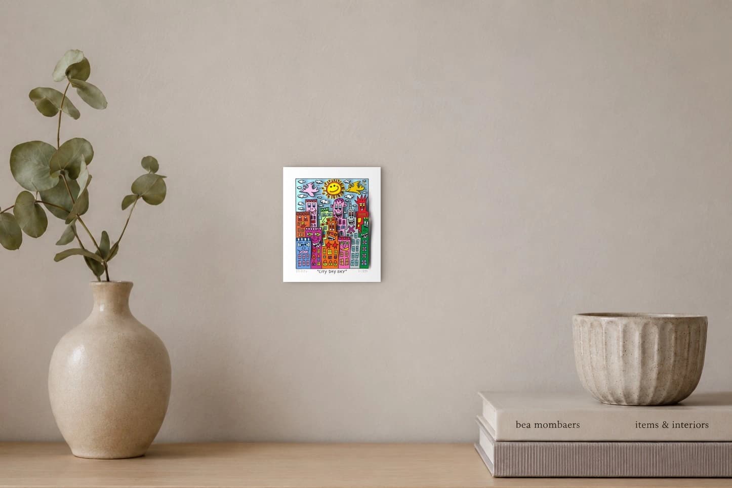 Bunte Häuser mit Gesichtern unter Sonne, Wolken und Vögeln, als Kunstwerk an der Wand eines hellen Raums.
