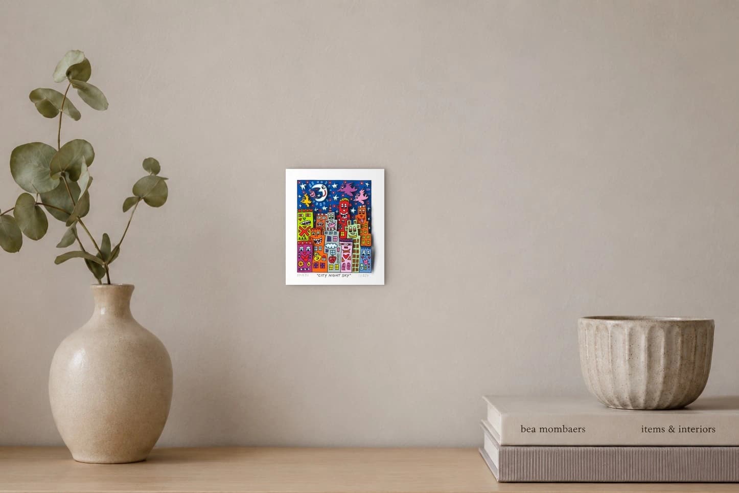 Bunte Häuser mit Gesichtern und Vögeln vor blauem Nachthimmel mit Mond und Sternen, als Kunstwerk an der Wand eines hellen Raums.