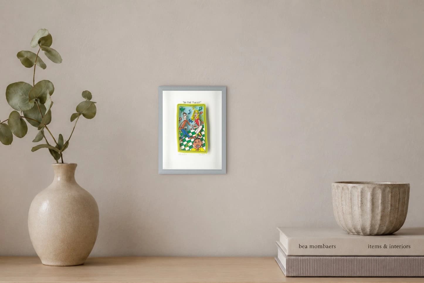 Vier Figuren tanzen in einem gelben Rahmen auf grün weißem Schachbrett unter „Do the Twist“, als Kunstwerk an der Wand eines hellen Raums.