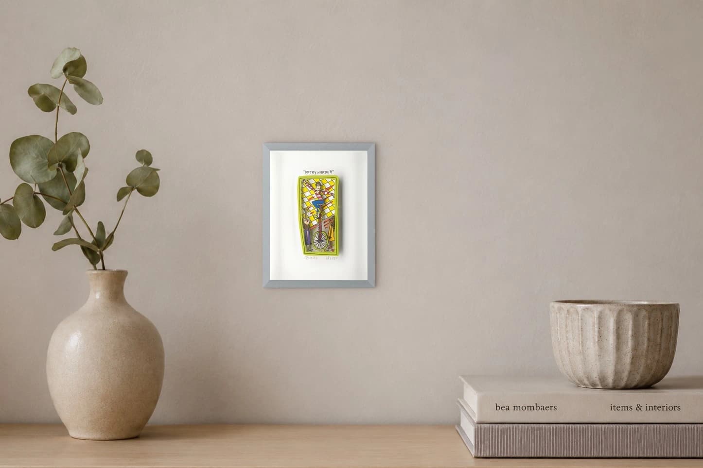 Gerahmtes Blatt mit gelb umrandetem Zirkusbild und dem Text „DO TRY HARDER“, als Kunstwerk an der Wand eines hellen Raums.