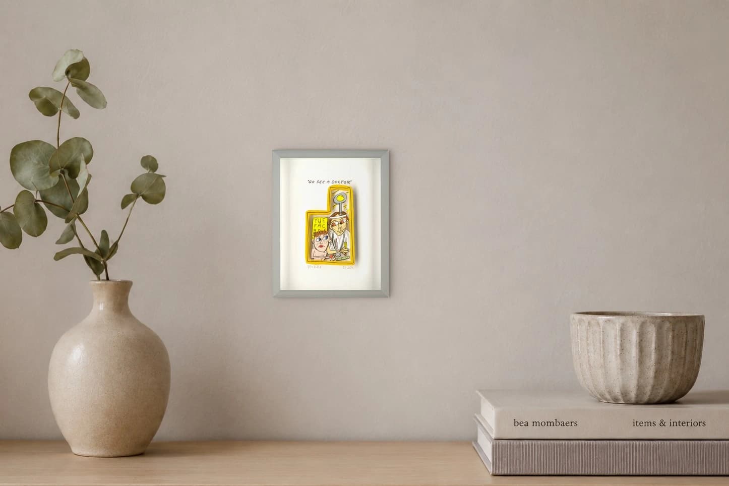 Gerahmtes Blatt mit Comicarzt und Kind im gelben Rahmen, oben steht „GO SEE A DOCTOR“, als Kunstwerk an der Wand eines hellen Raums.