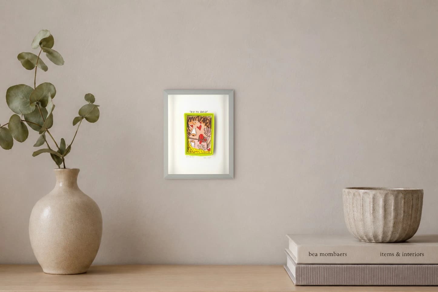 Gerahmtes Bild mit Comicgesicht im gelben Rahmen, darüber GO TO BED und unten Rizzi, als Kunstwerk an der Wand eines hellen Raums.