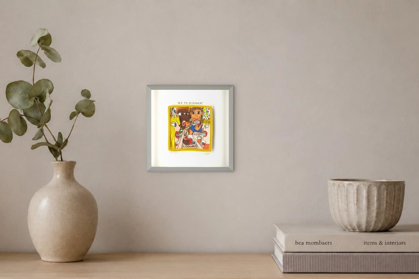 Gerahmtes Bild mit fünf Gesichtern am Tisch, oben der Text "GO TO DINNER" und viele Speisen, als Kunstwerk an der Wand eines hellen Raums.