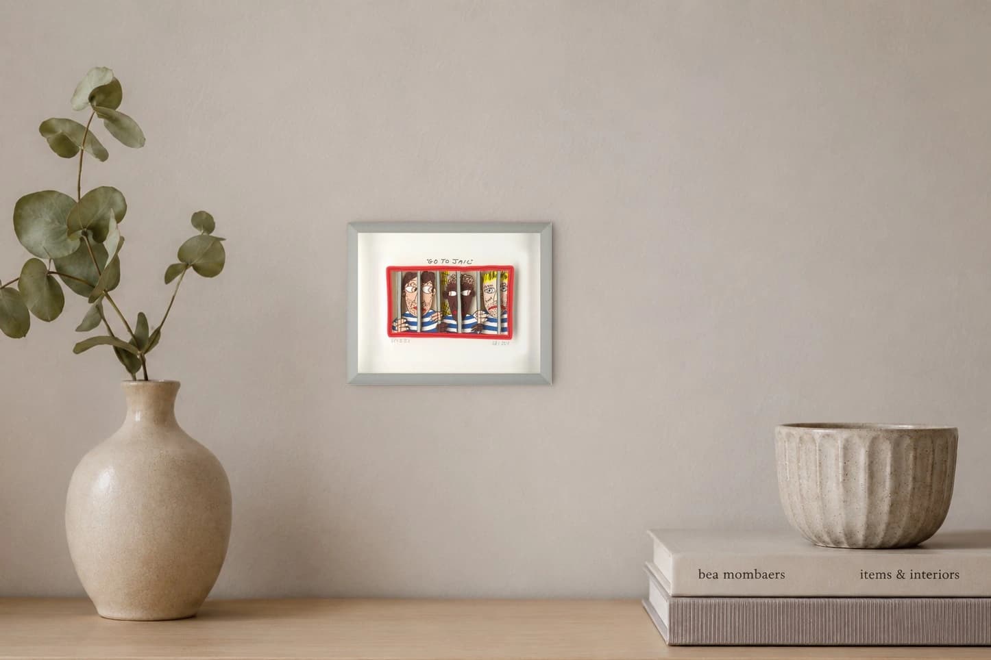 Gerahmtes Bild mit drei Männern hinter Gittern und dem Text „GO TO JAIL“, als Kunstwerk an der Wand eines hellen Raums.