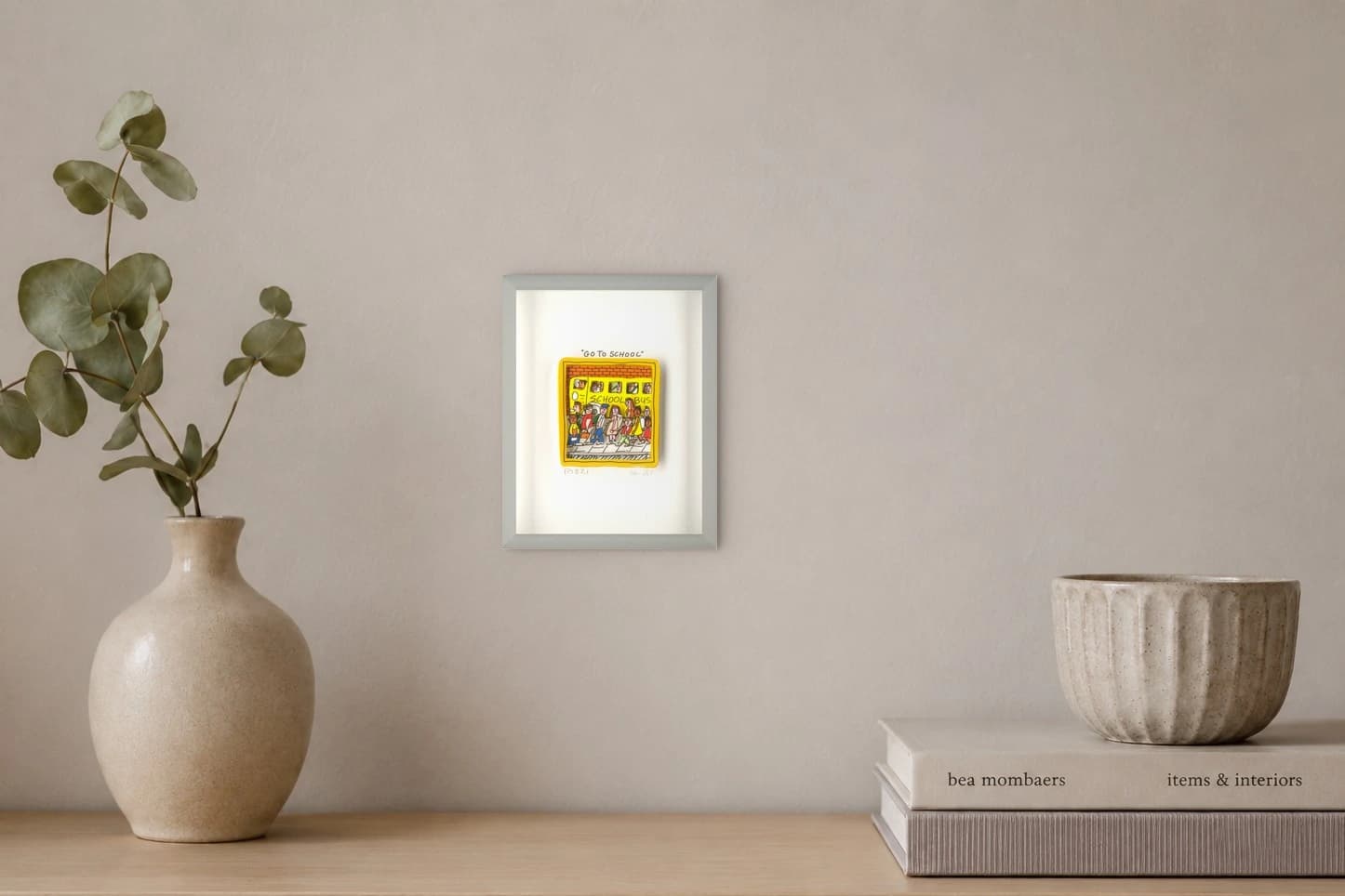 Gerahmte Zeichnung eines gelben Schulbusses mit Kindern vor einer Backsteinwand auf weißem Hintergrund, als Kunstwerk an der Wand eines hellen Raums.