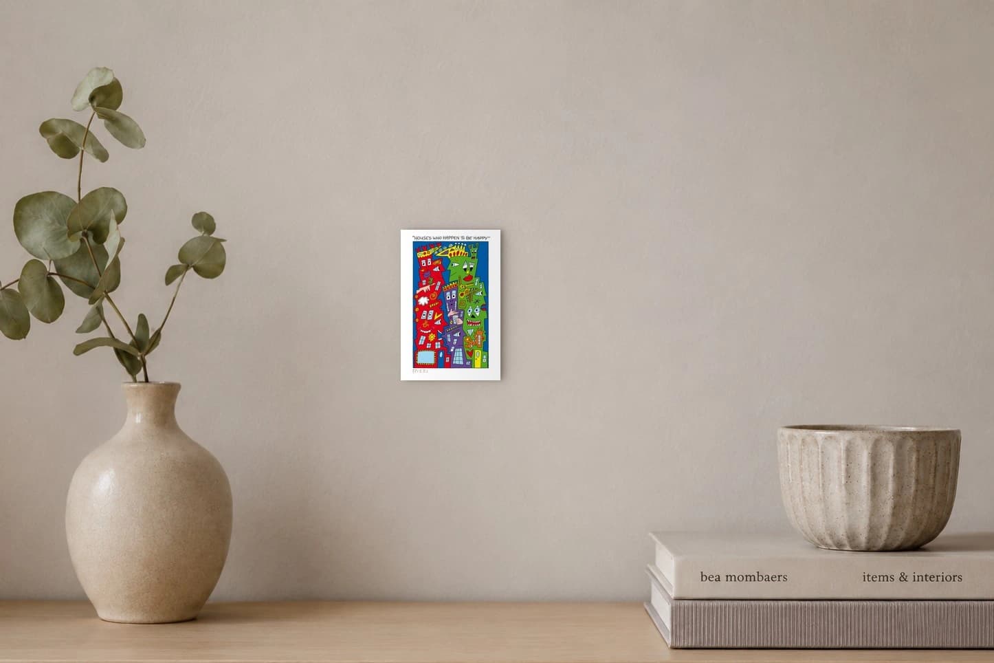 Bunte Häuser mit Gesichtern vor blauem Hintergrund und dem Schriftzug „Houses Who Happen to Be Happy“, als Kunstwerk an der Wand eines hellen Raums.
