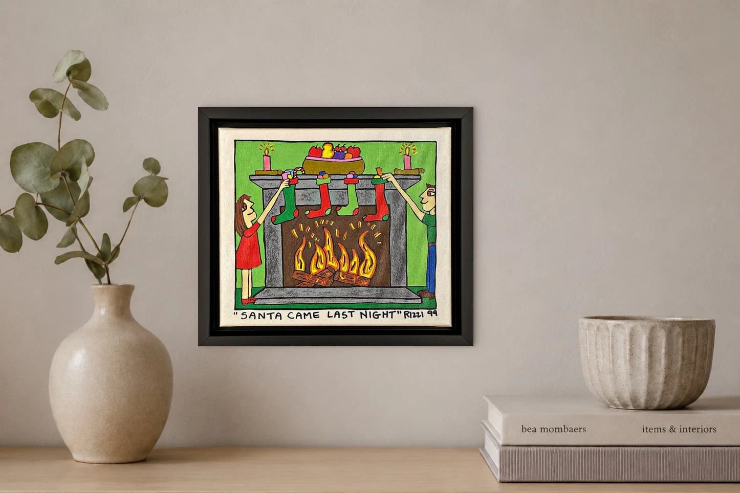 Gerahmtes Bild mit zwei Kindern am Kamin, Socken, Kerzen, Geschenken und Feuer, unten steht Santa Came Last Night, als Kunstwerk an der Wand eines hellen Raums.
