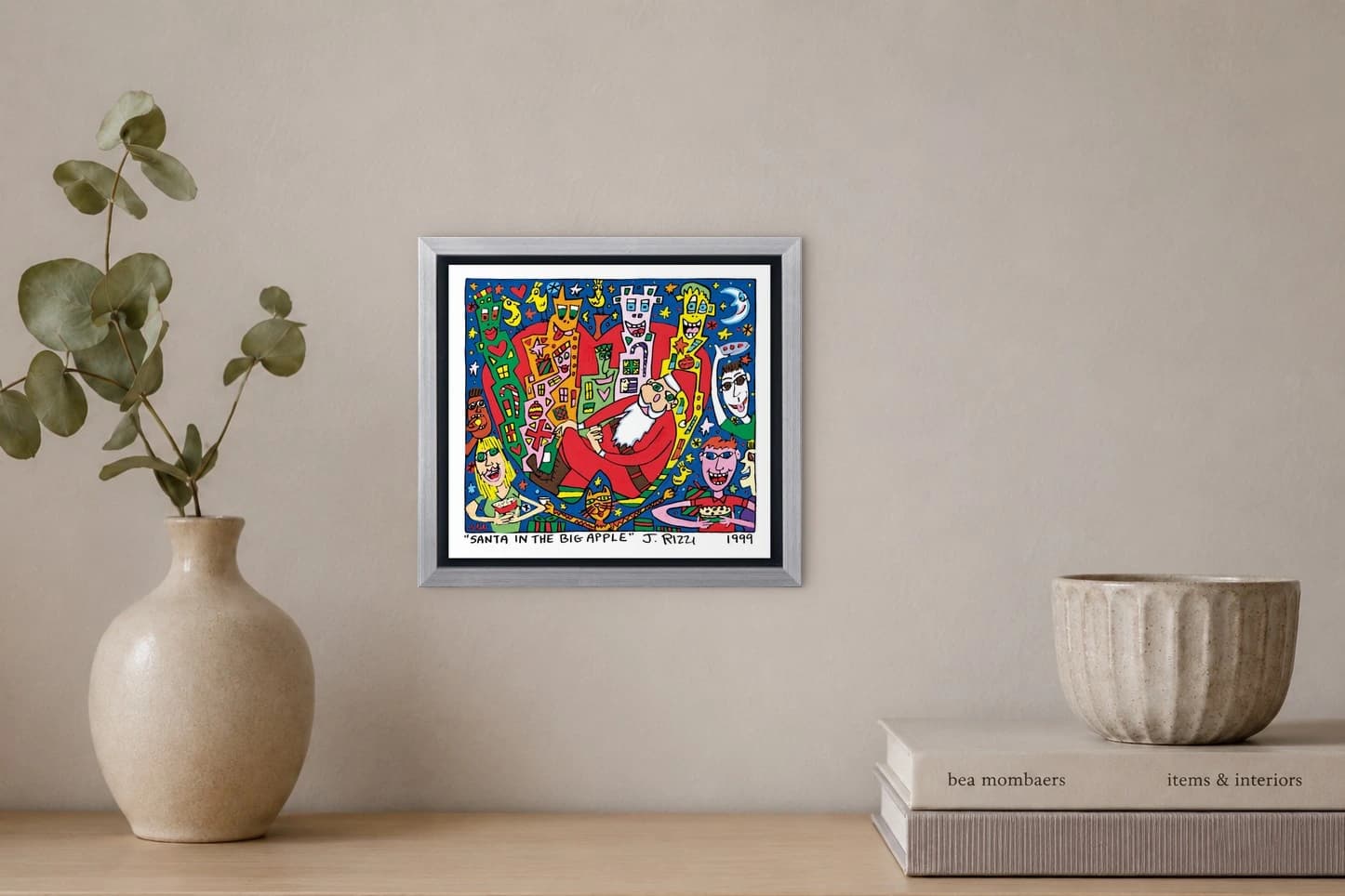 Gerahmtes Bild mit Santa im roten Anzug, bunten Gesichtern und Figuren vor blauem Himmel, als Kunstwerk an der Wand eines hellen Raums.
