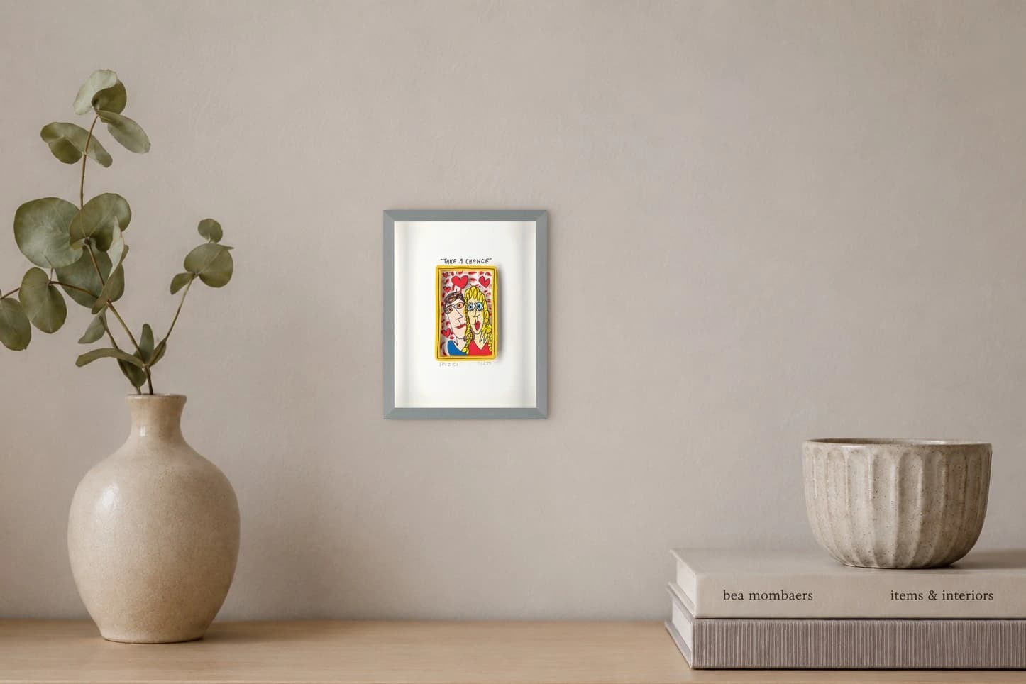 Gerahmtes Blatt mit gelbem Rahmen, zwei gezeichneten Köpfen, Herzen und TAKE A CHANCE, als Kunstwerk an der Wand eines hellen Raums.
