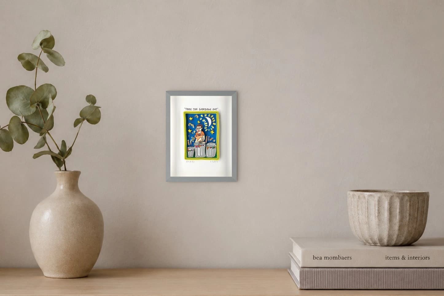 Gerahmtes Blatt mit „TAKE THE GARBAGE OUT“, Figur zwischen drei Mülltonnen vor blauem Himmel, als Kunstwerk an der Wand eines hellen Raums.