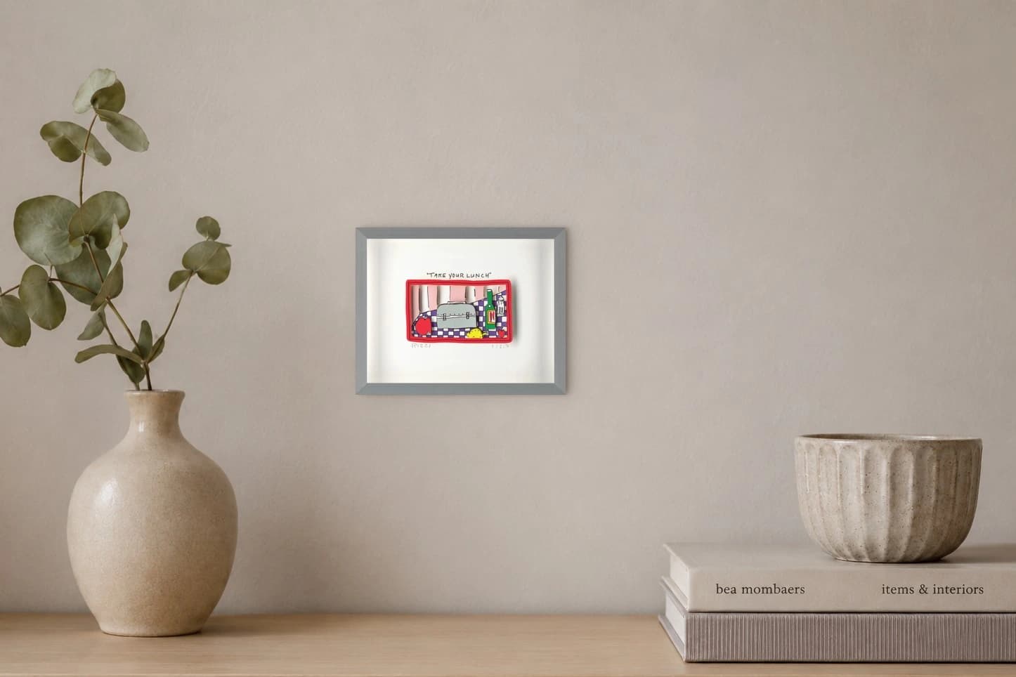 Gerahmtes Blatt mit roter Tasche, Tomate, Brotbox, grünem Flaschenmotiv und „TAKE YOUR LUNCH“, als Kunstwerk an der Wand eines hellen Raums.