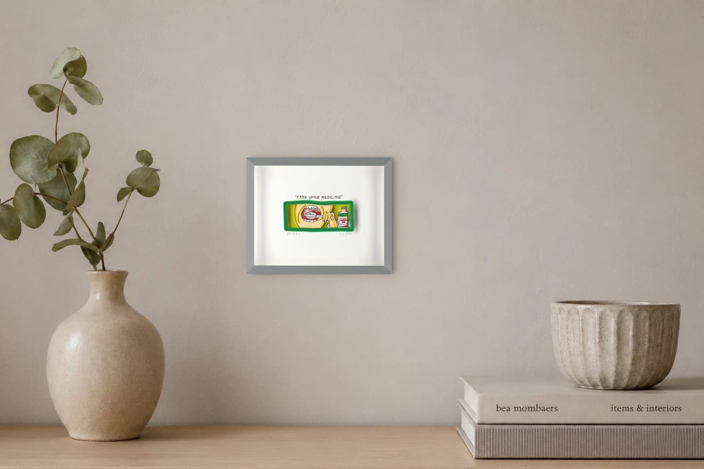 Gerahmtes Bild mit Mund und Löffel vor einer pinken Flasche und dem Text Take your medicine, als Kunstwerk an der Wand eines hellen Raums.