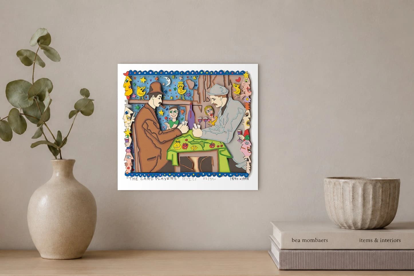 Zwei Männer spielen Karten am Tisch, umgeben von bunten Gesichtern, Sternen und Vögeln im Rahmen, als Kunstwerk an der Wand eines hellen Raums.