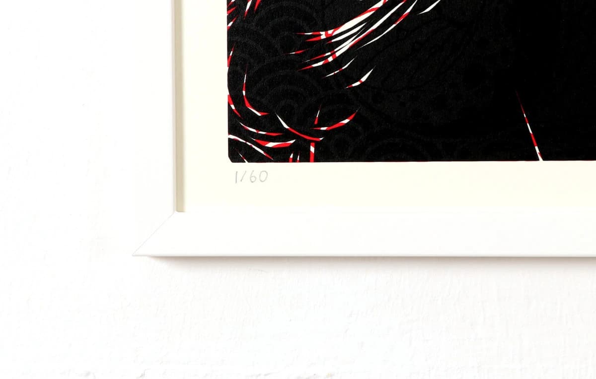 Gerahmtes Bild mit schwarzem, rot-weißem Motiv hängt an weißer Wand, links mit hellem Rand.