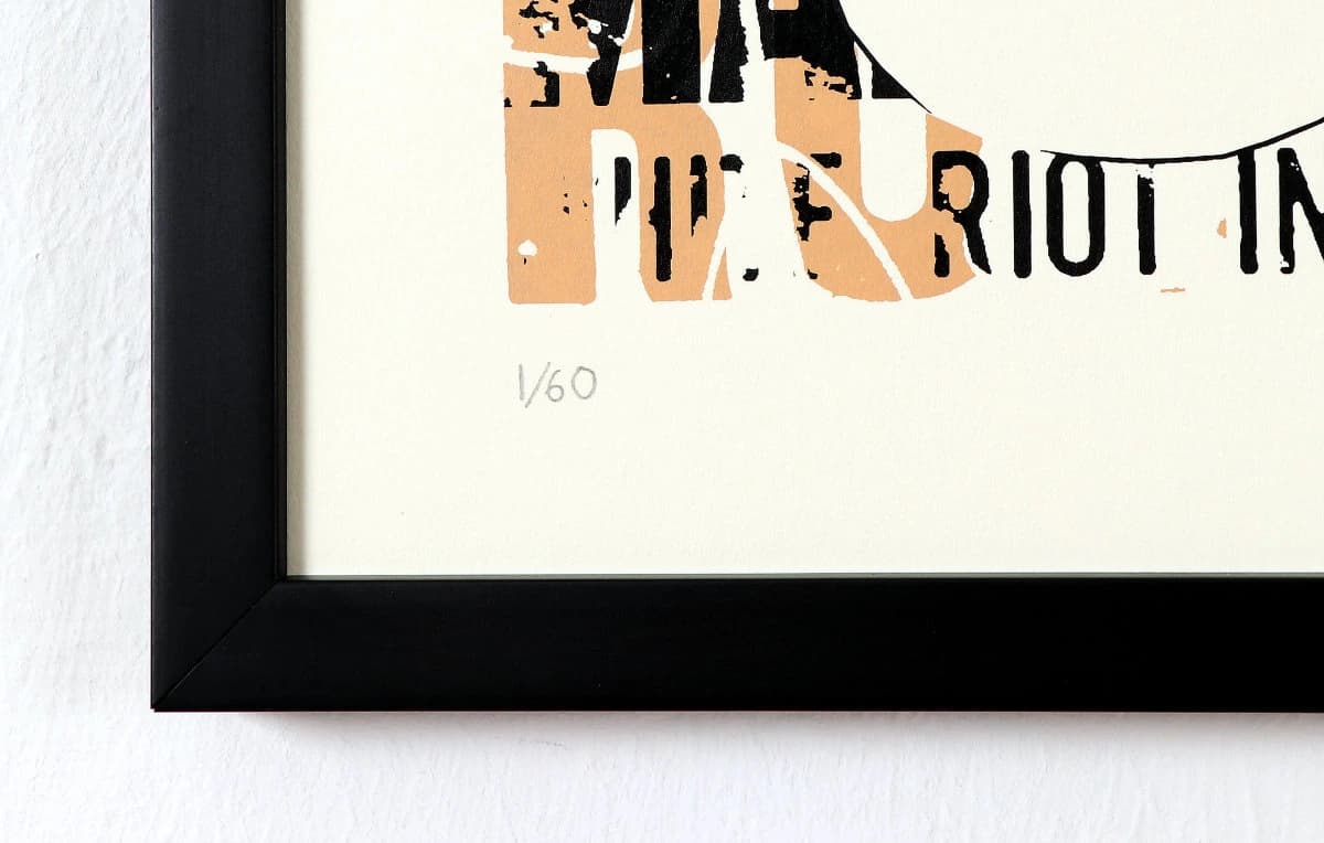 Gerahmtes Bild mit abgeschnittenem Schwarz-Beige-Schriftzug auf weißem Papier, an heller Wand.