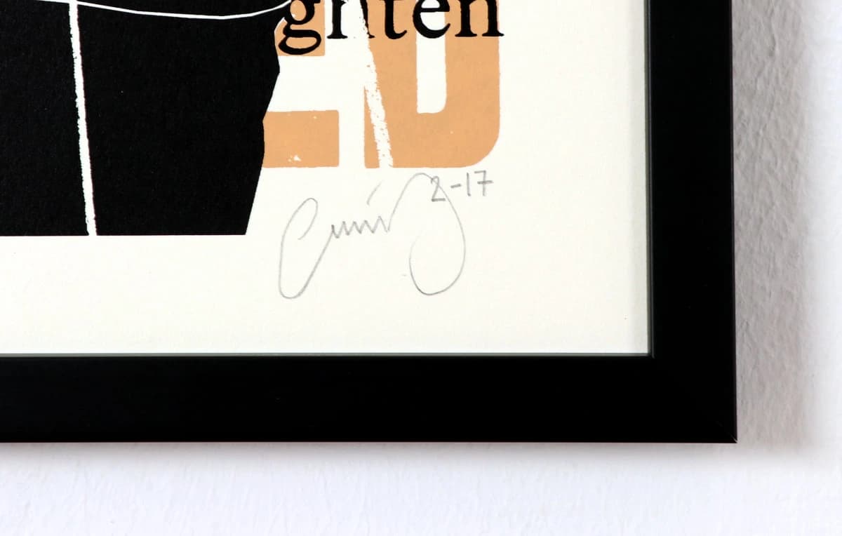 Gerahmtes Plakat mit schwarzem und beigem Motiv, Signatur und schwarzem Rahmen an weißer Wand.