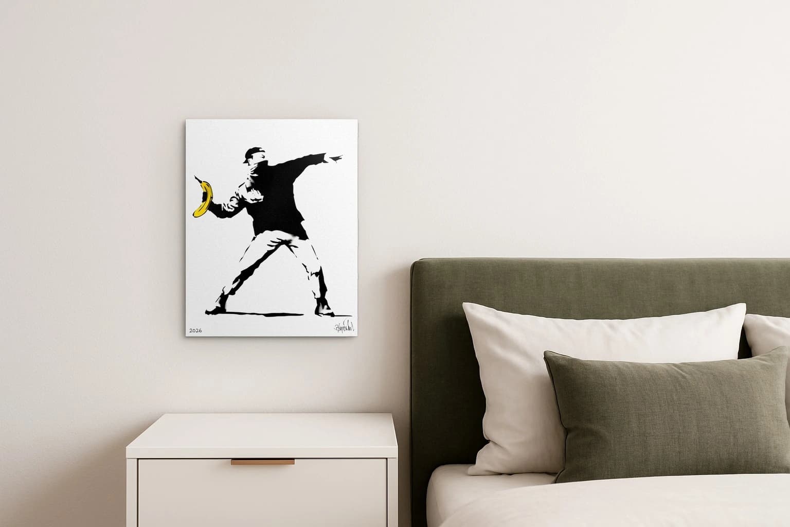 Schwarze Figur wirft eine gelbe Banane vor weißem Hintergrund mit 2026 und Signatur, als Kunstwerk an der Wand eines Schlafzimmers.