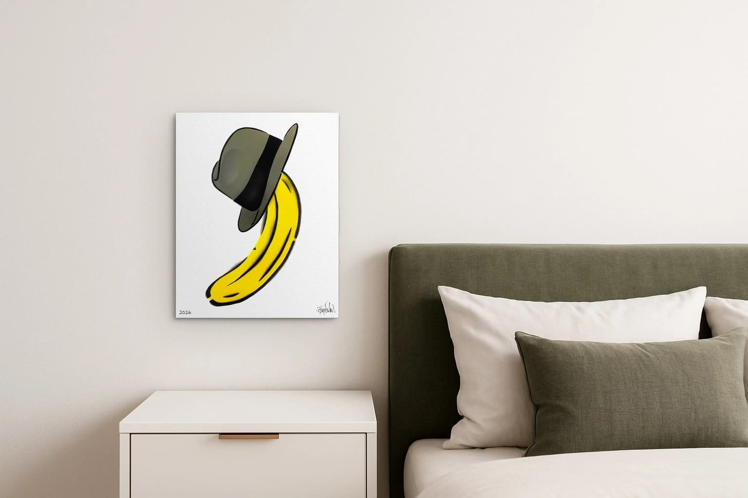 Gelbe Banane mit grauem Hut auf Weiß, unten links 2026 und rechts Signatur, als Kunstwerk an der Wand eines Schlafzimmers.