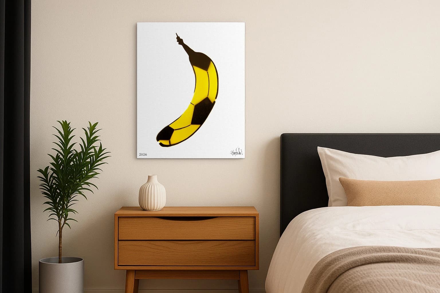 Gelbe Banane mit schwarzen Flächen auf weißem Hintergrund, unten links 2026 und unten rechts Signatur, als Kunstwerk an der Wand eines Schlafzimmers.
