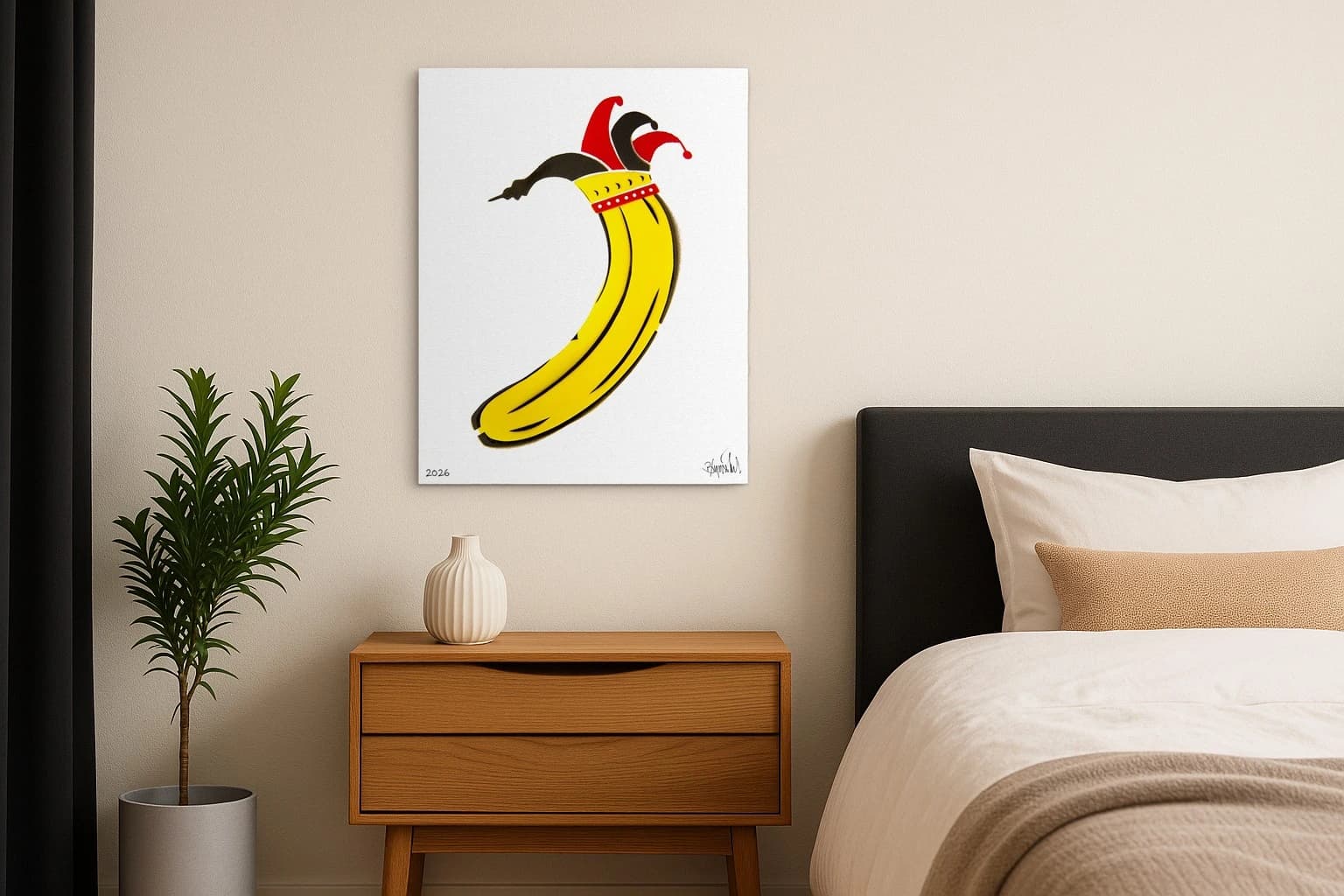 Gelbe Banane mit roter und schwarzer Narrenkappe auf weißem Papier, als Kunstwerk an der Wand eines Schlafzimmers.