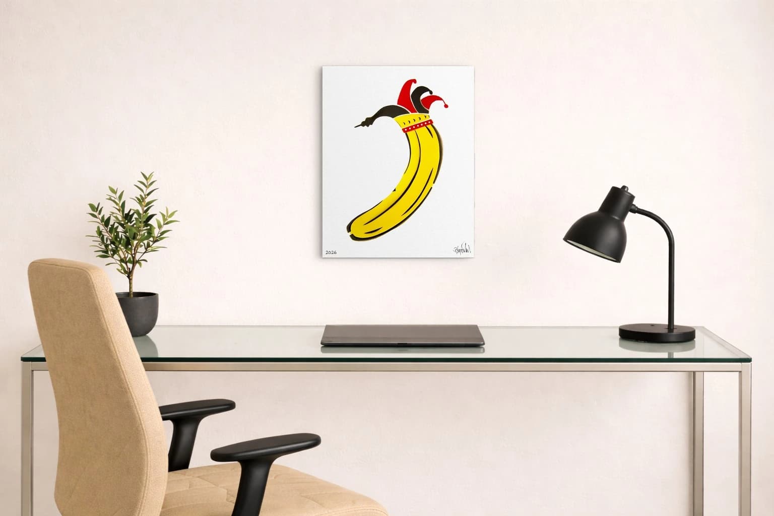 Gelbe Banane mit roter und schwarzer Narrenkappe auf weißem Papier, als Kunstwerk an der Wand eines Arbeitszimmers.