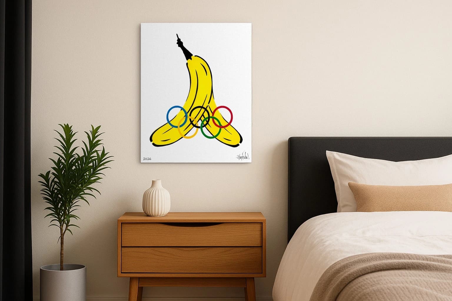 Gelbe Banane mit Olympischen Ringen, unten links 2026 und Signatur, als Kunstwerk an der Wand eines Schlafzimmers.