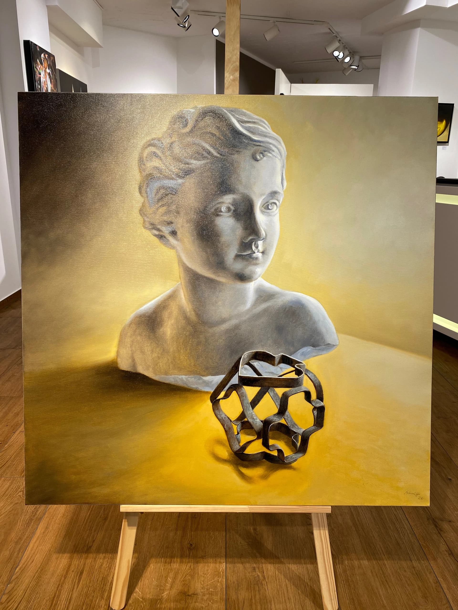 Büste einer jungen Frau auf gelbem Grund, davor ein schwarzes geometrisches Metallobjekt auf einer Staffelei im Ausstellungsraum.