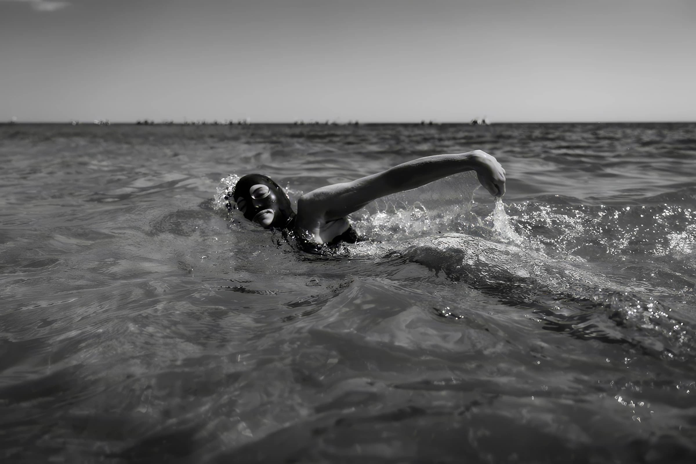 Eine Person schwimmt im Meer im Vordergrund, mit ruhiger Wasseroberfläche und Horizont im Hintergrund.