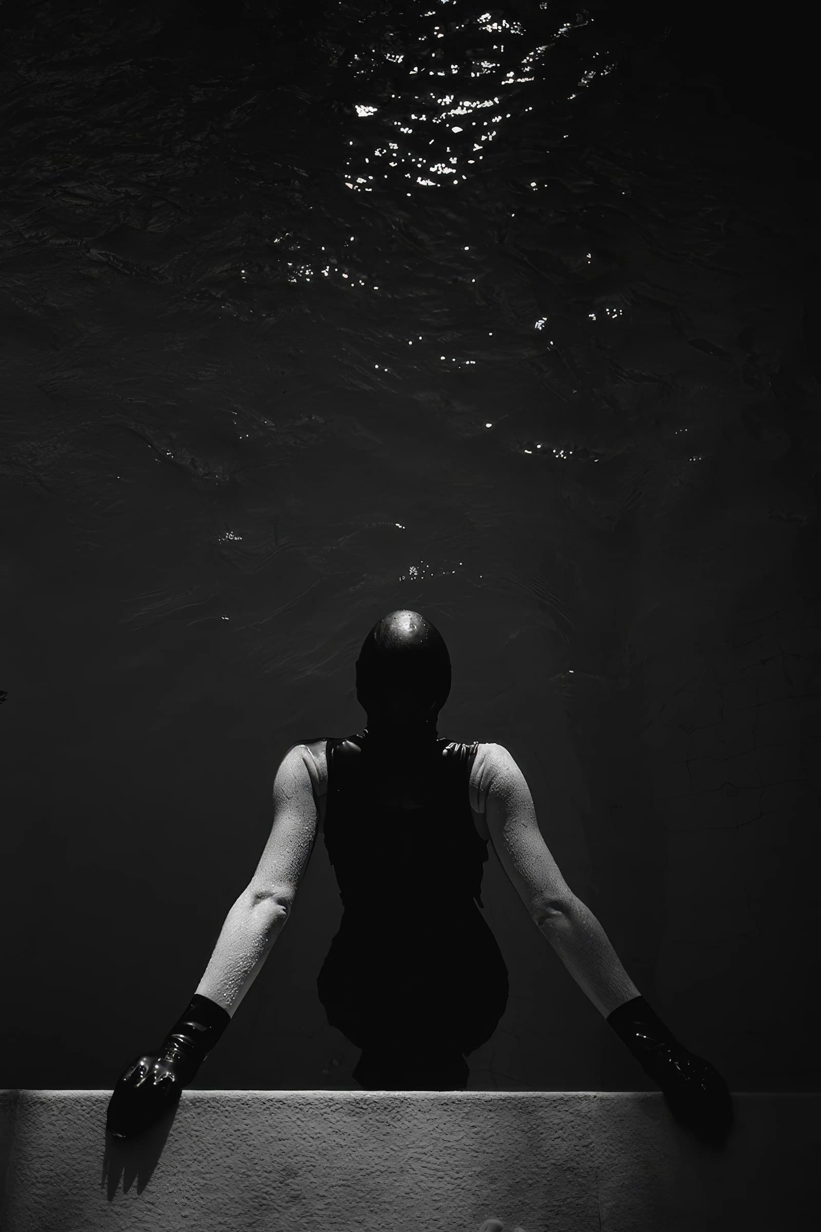 Dunkle Person im schwarzen Anzug lehnt an einer Mauer im Wasser, darüber spiegelnde Wellen.