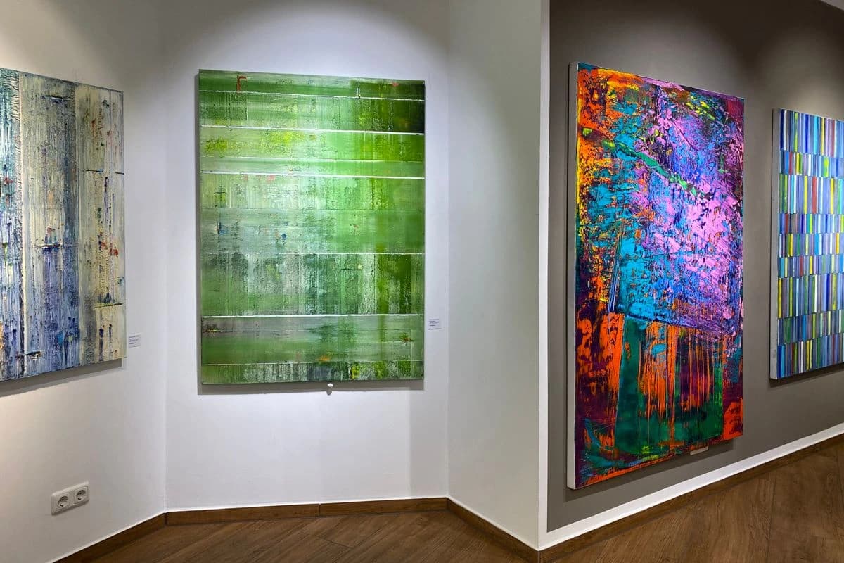 Vier abstrakte Gemälde hängen in einer Galerie mit weißen und grauen Wänden sowie Holzboden.